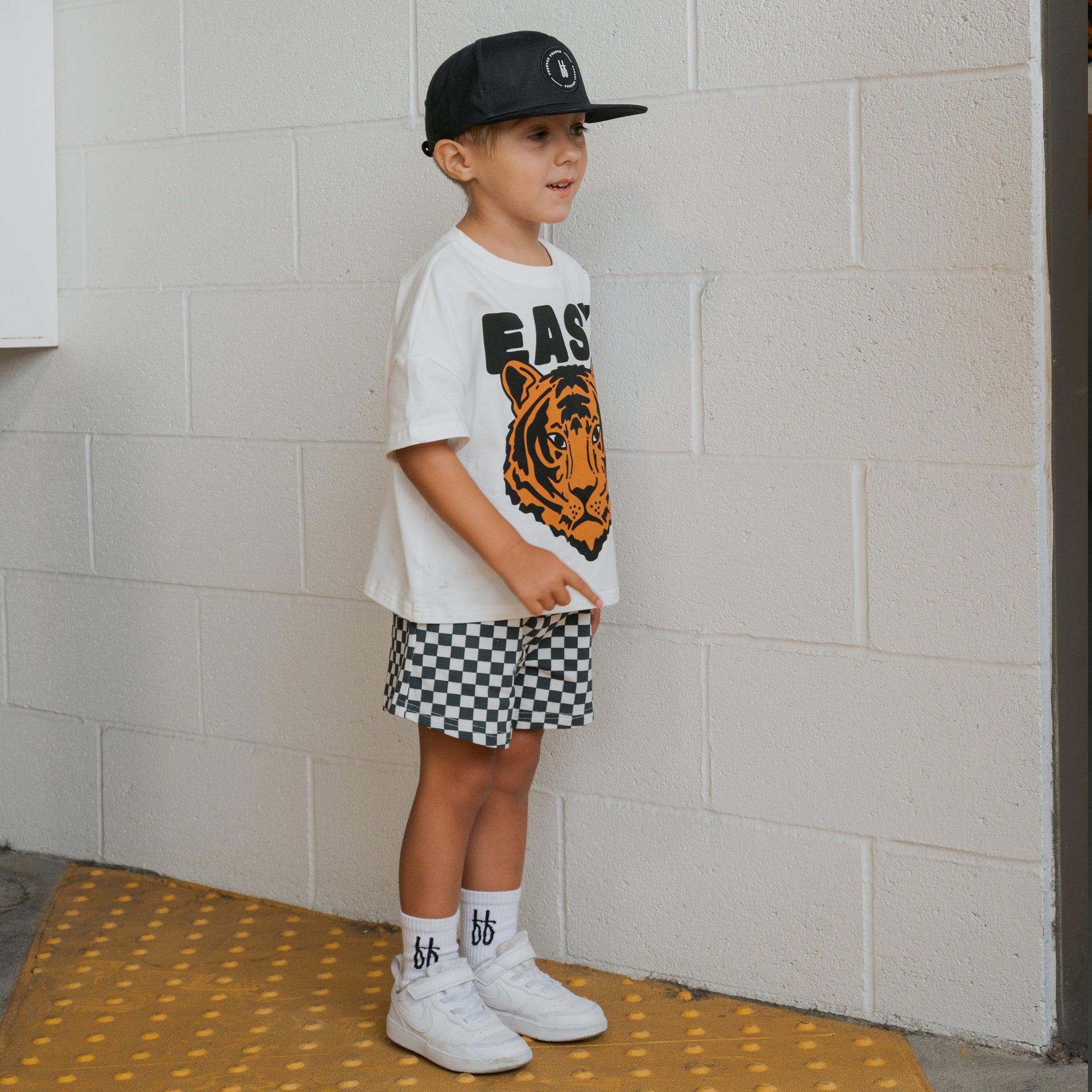 Child wearing an Easy Tiger graphic crew neck top and coordinating checkered shorts set outdoors.