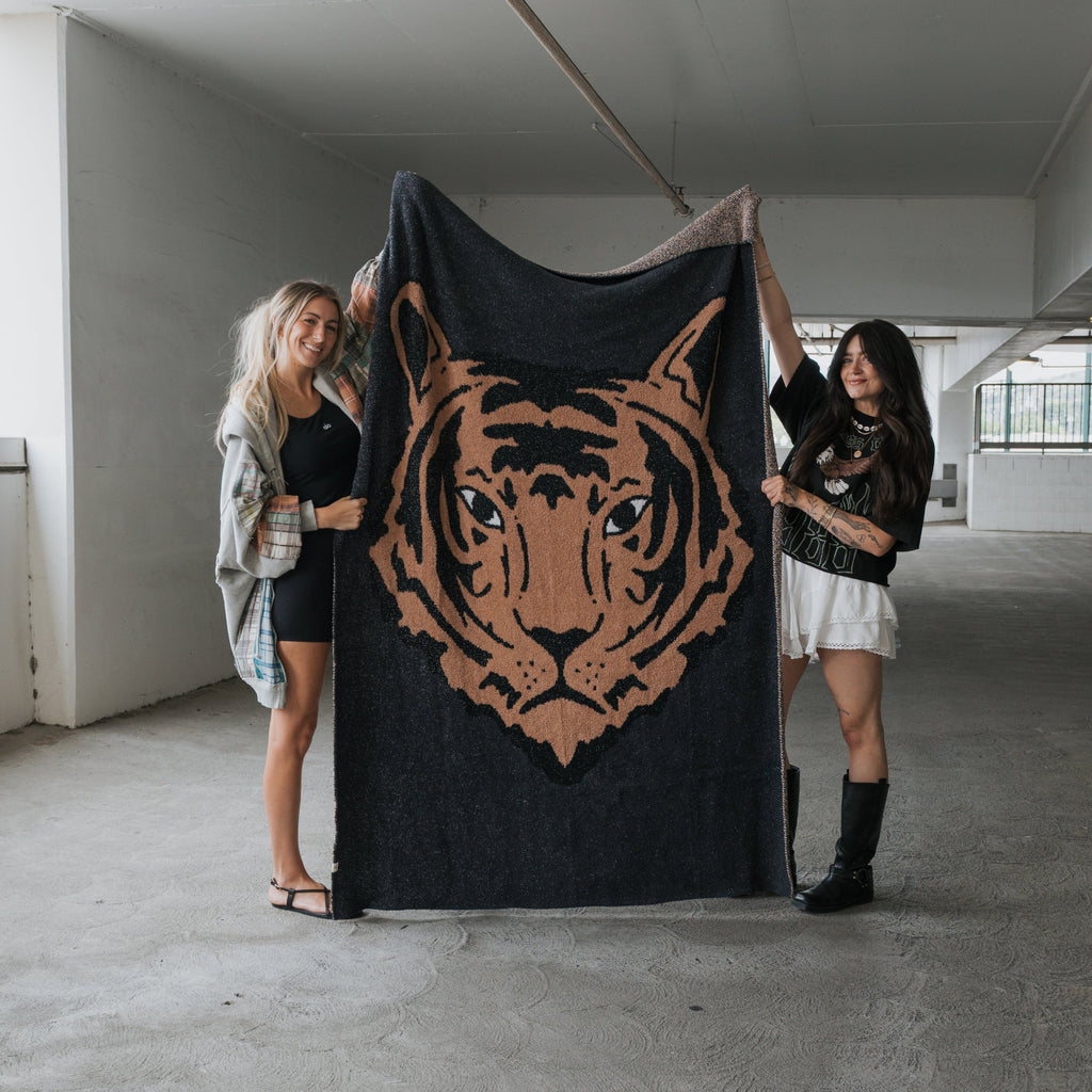 A plush black and camel tiger print knit throw blanket draped over a modern sofa in a cozy living room setting.