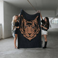 A plush black and camel tiger print knit throw blanket draped over a modern sofa in a cozy living room setting.