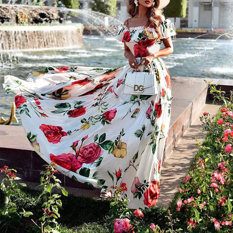 A woman wearing a white off-shoulder maxi dress with a vibrant red and yellow rose print standing in front of a fountain.