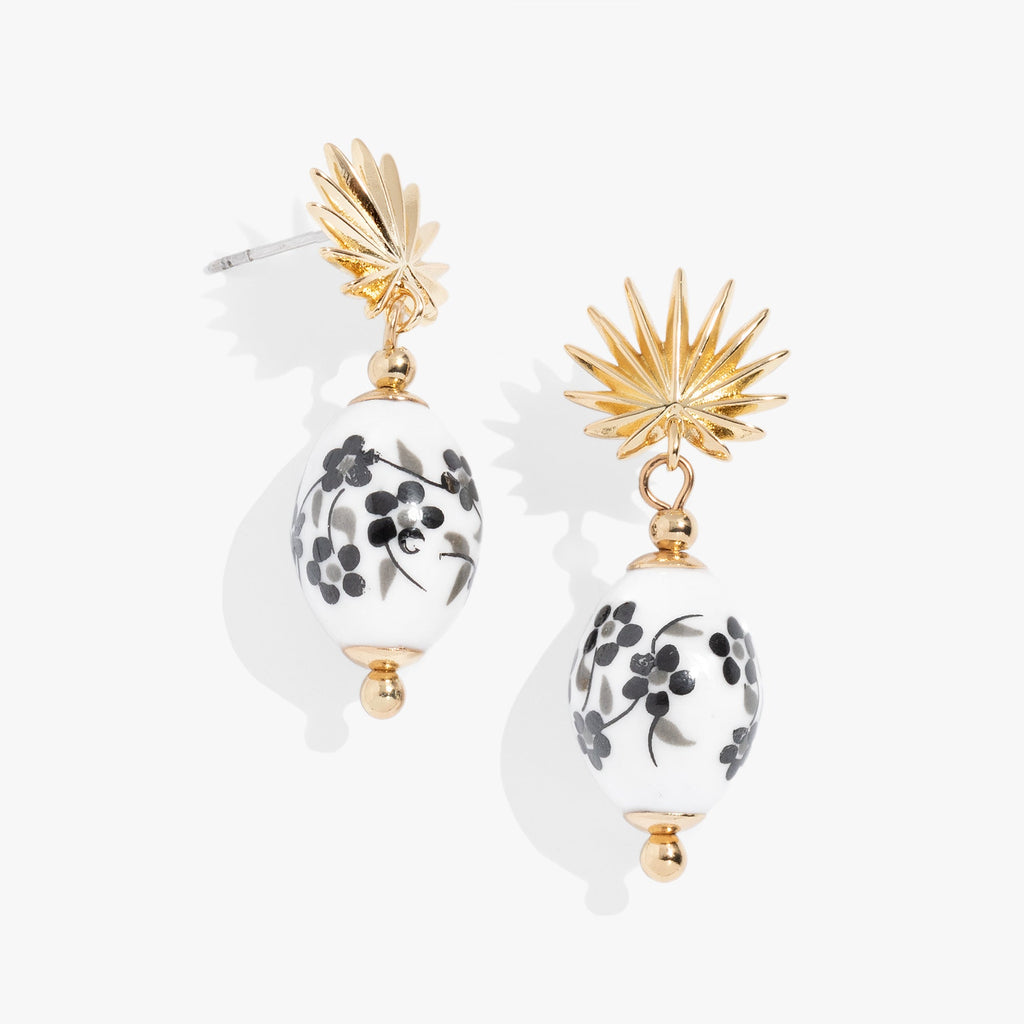 Close up of Toile and Palm Drop Earrings with monochrome floral pattern and polished gold-tone palm frond accents.