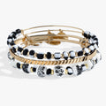 Set of three bangles featuring one hand-painted toile floral pattern, one black and white glass beaded bangle, and one gold-tone textured bangle.