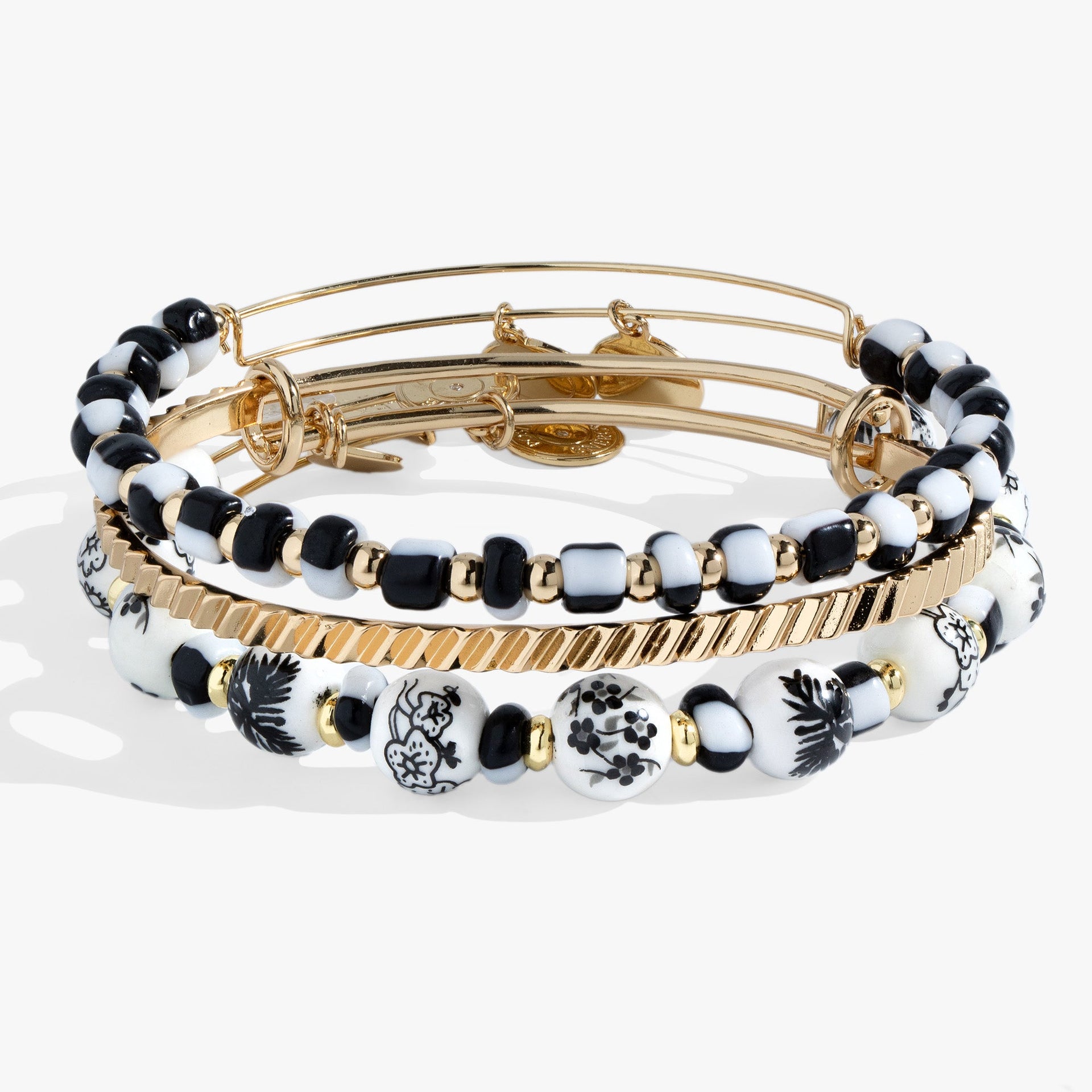 Set of three bangles featuring one hand-painted toile floral pattern, one black and white glass beaded bangle, and one gold-tone textured bangle.