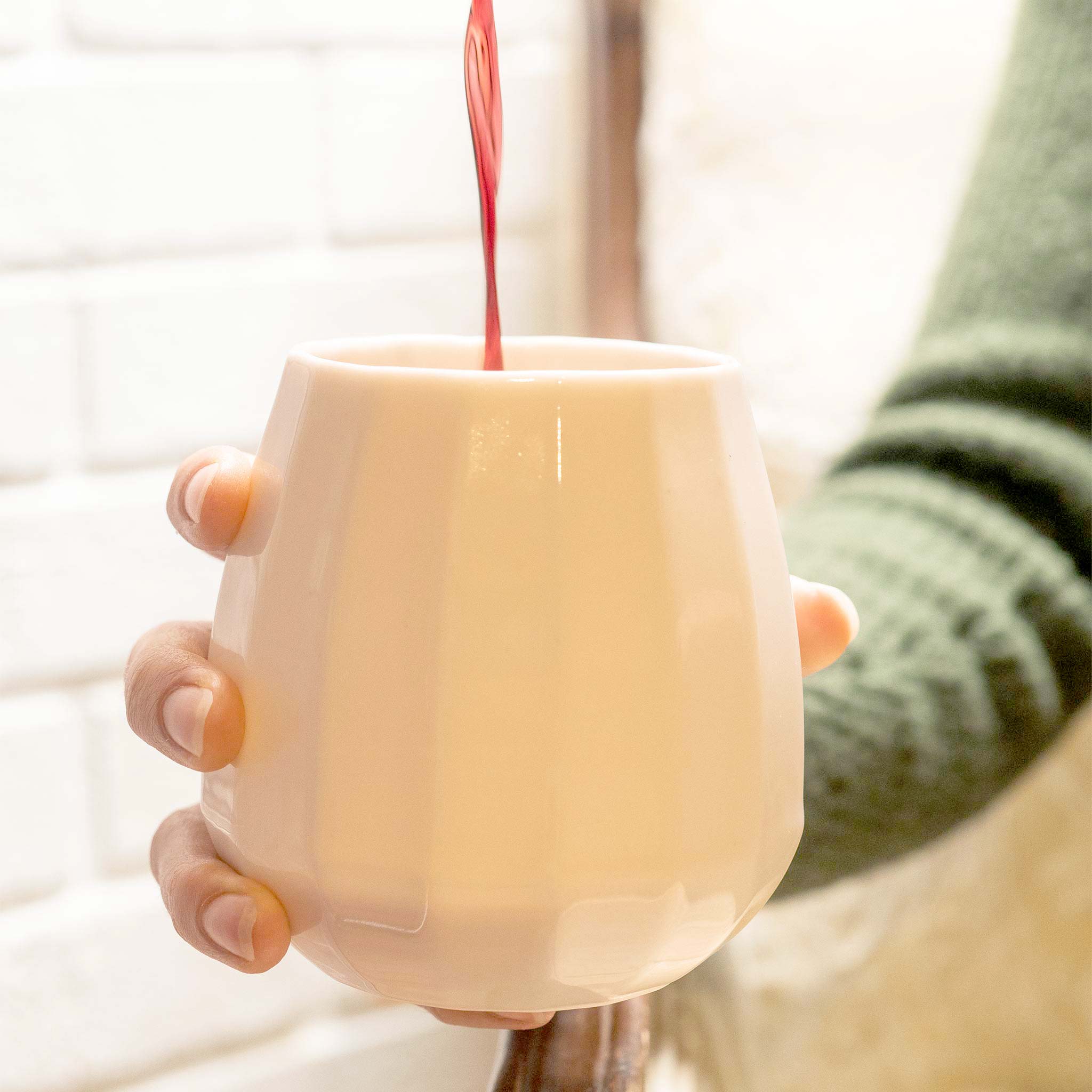 Handmade light cream porcelain wine glass being filled with red wine