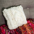 Off-white triple cable knit small square throw pillow on a minimalist neutral sofa
