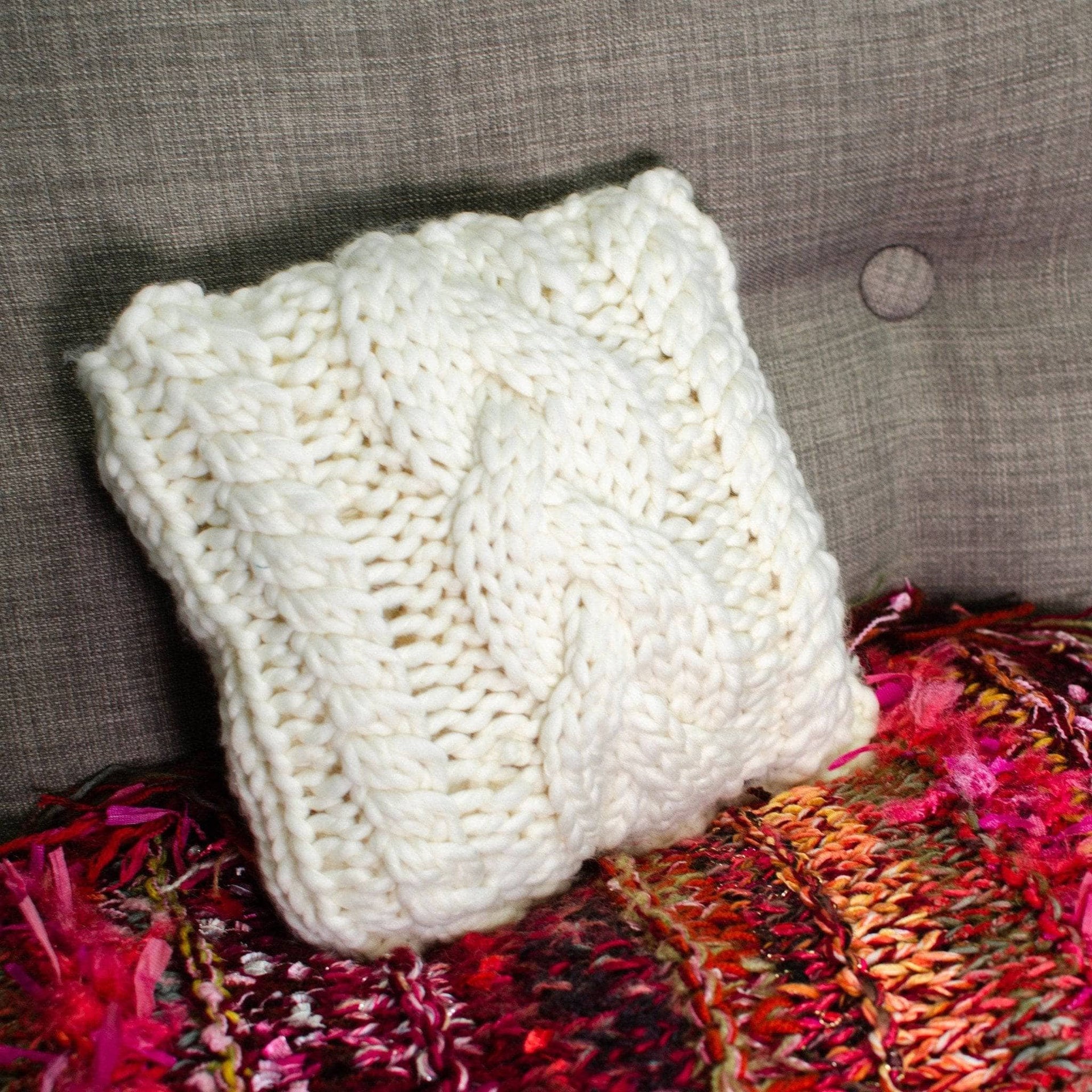 Off-white triple cable knit small square throw pillow on a minimalist neutral sofa