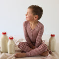 A young boy wearing a red and white window pane patterned two-piece bamboo pajama set while sitting on a blanket.