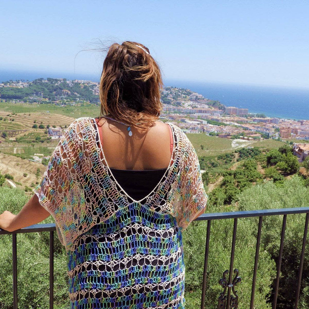 Woman wearing an oversized blue, green, and cream crochet duster in a coastal-resort setting.