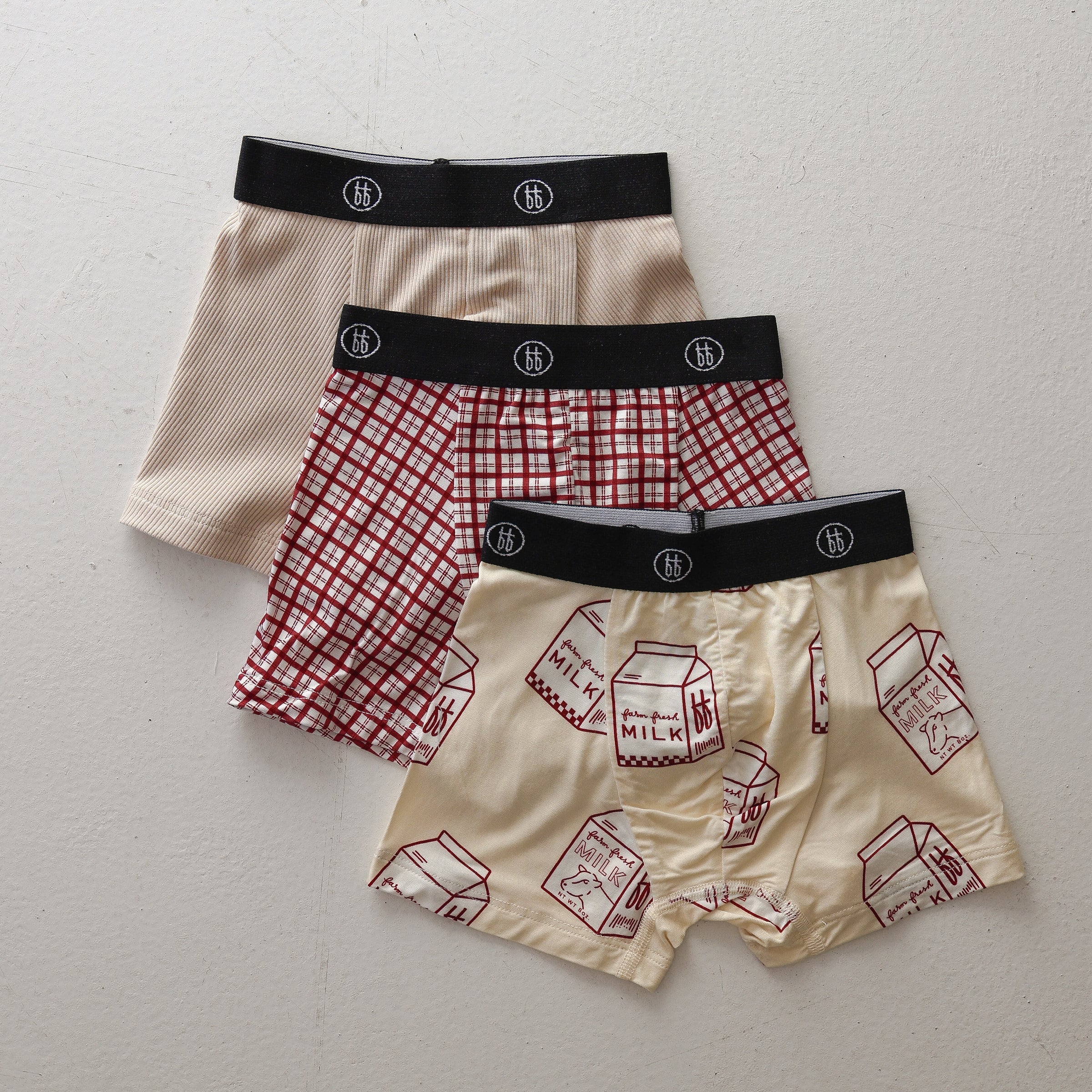 Three pairs of kids boxer briefs in window pane, milk carton, and ribbed cream prints with black branded elastic waistbands.