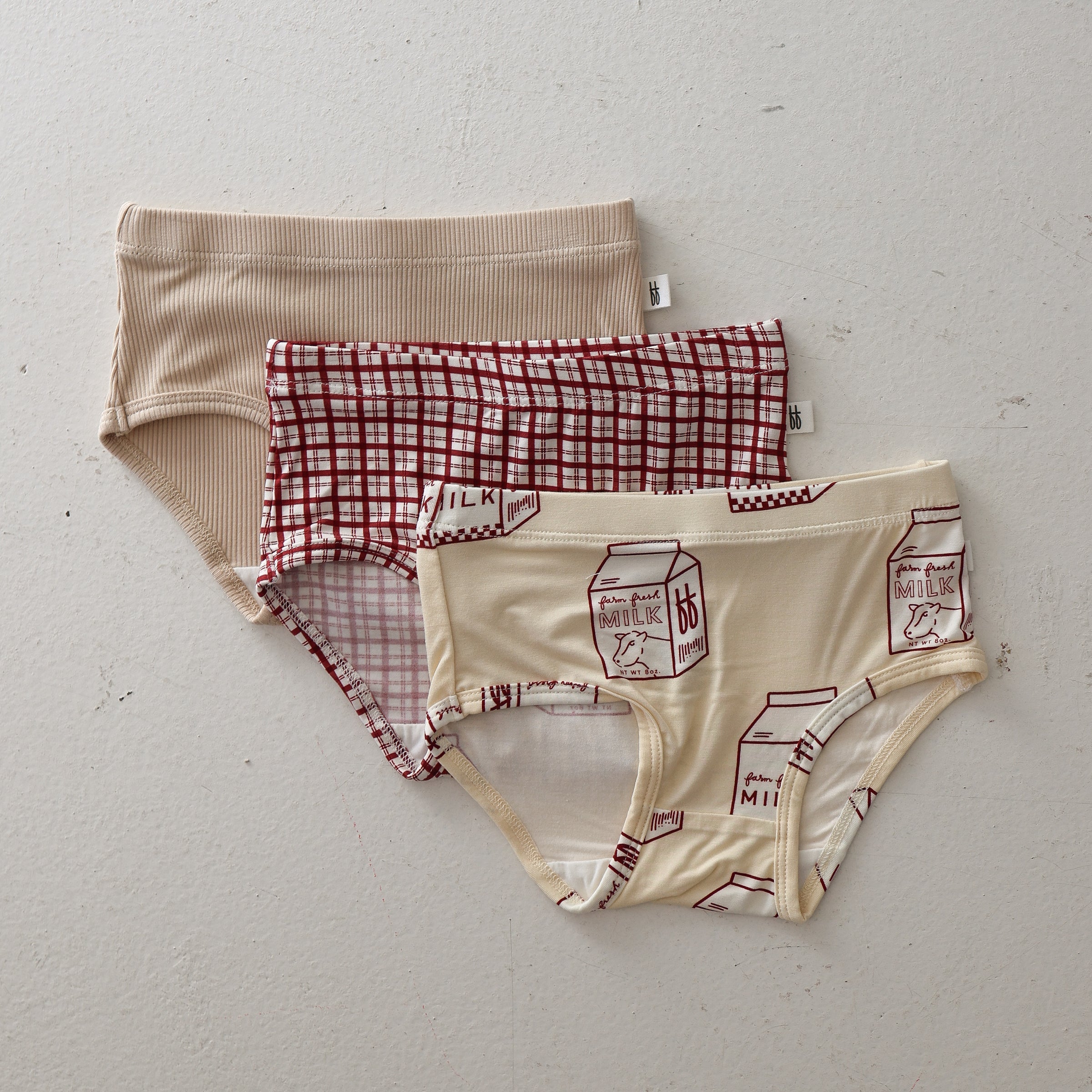 Three-pack of girls' bamboo briefs in cream ribbed fabric, red window pane pattern, and milk carton print.