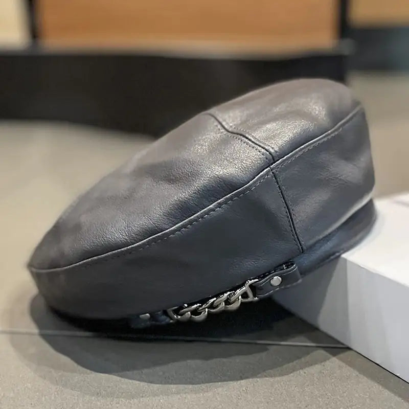 Close-up of a stylish women's PU leather beret in brown and grey featuring a metallic chain detail on the side.
