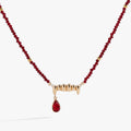 Close up of a gothic vampire fangs pendant with a red siam crystal drop on a gold chain.