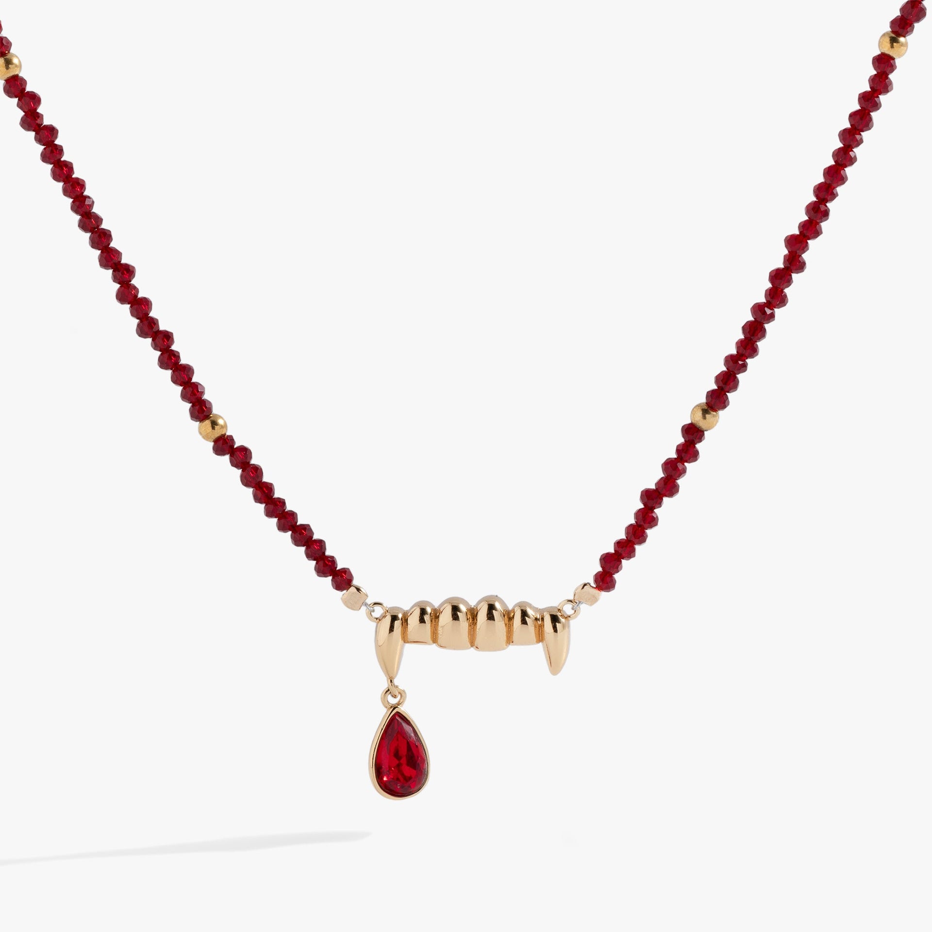 Close up of a gothic vampire fangs pendant with a red siam crystal drop on a gold chain.