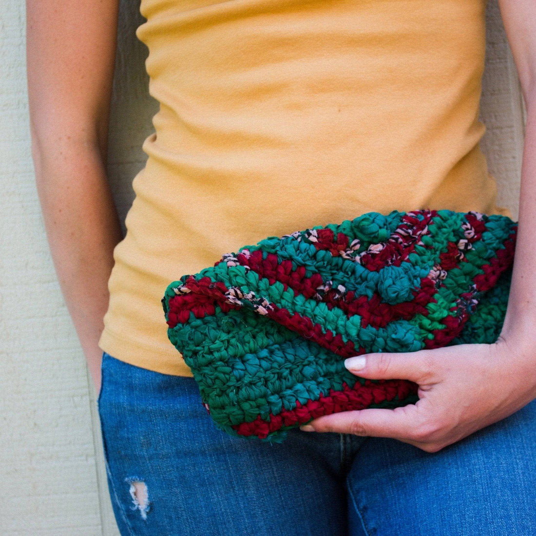 Vibrant teal and maroon striped knit crochet clutch held as a boho fashion accessory