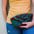 Vibrant teal and maroon striped knit crochet clutch held as a boho fashion accessory