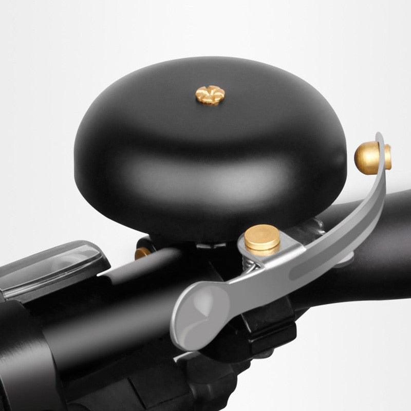Vintage classic bicycle bell in metallic gold and matte black finish mounted on a bike handlebar