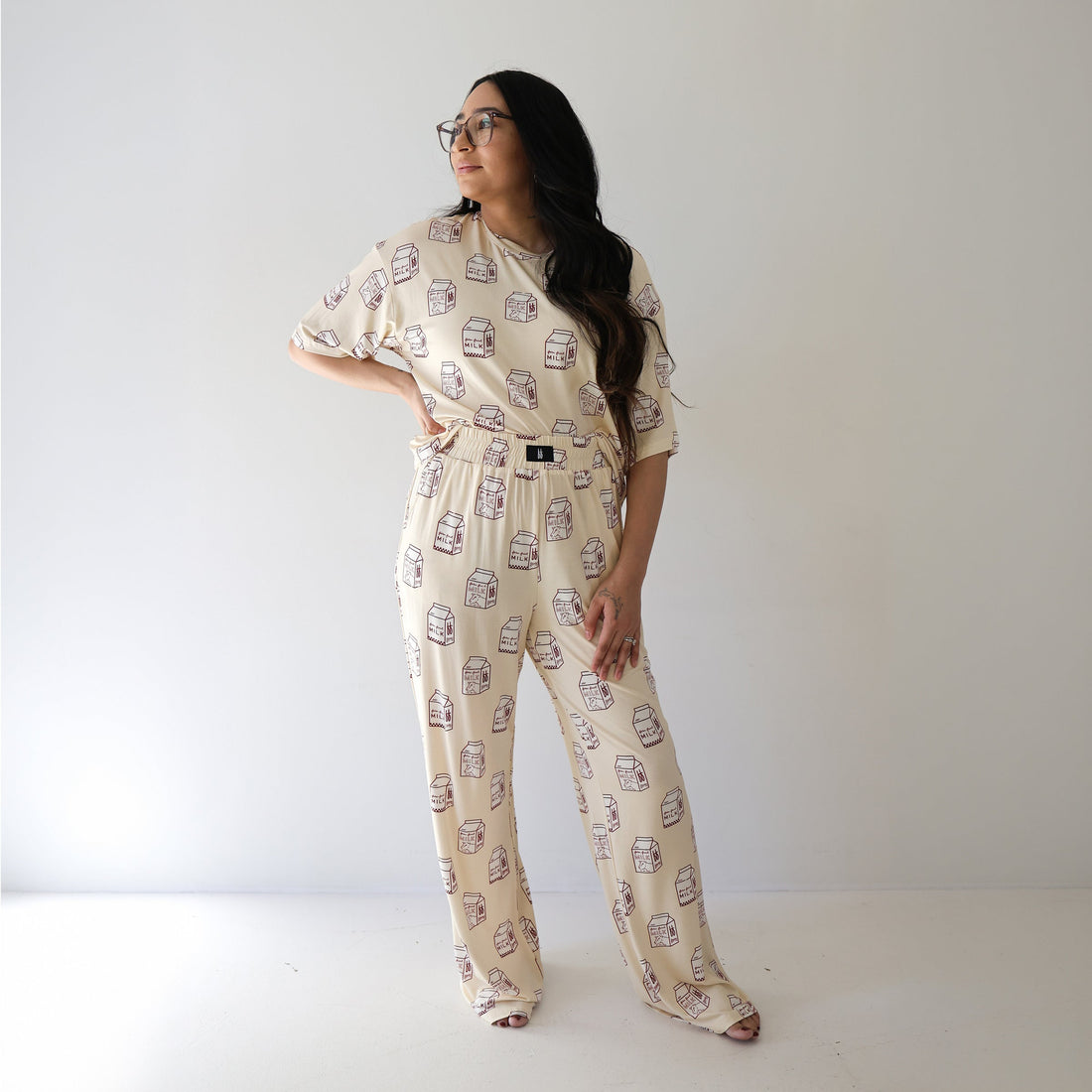 A woman wearing a beige matching lounge set with a milk carton print, consisting of a short-sleeved boxy tee and wide-leg lounge pants.
