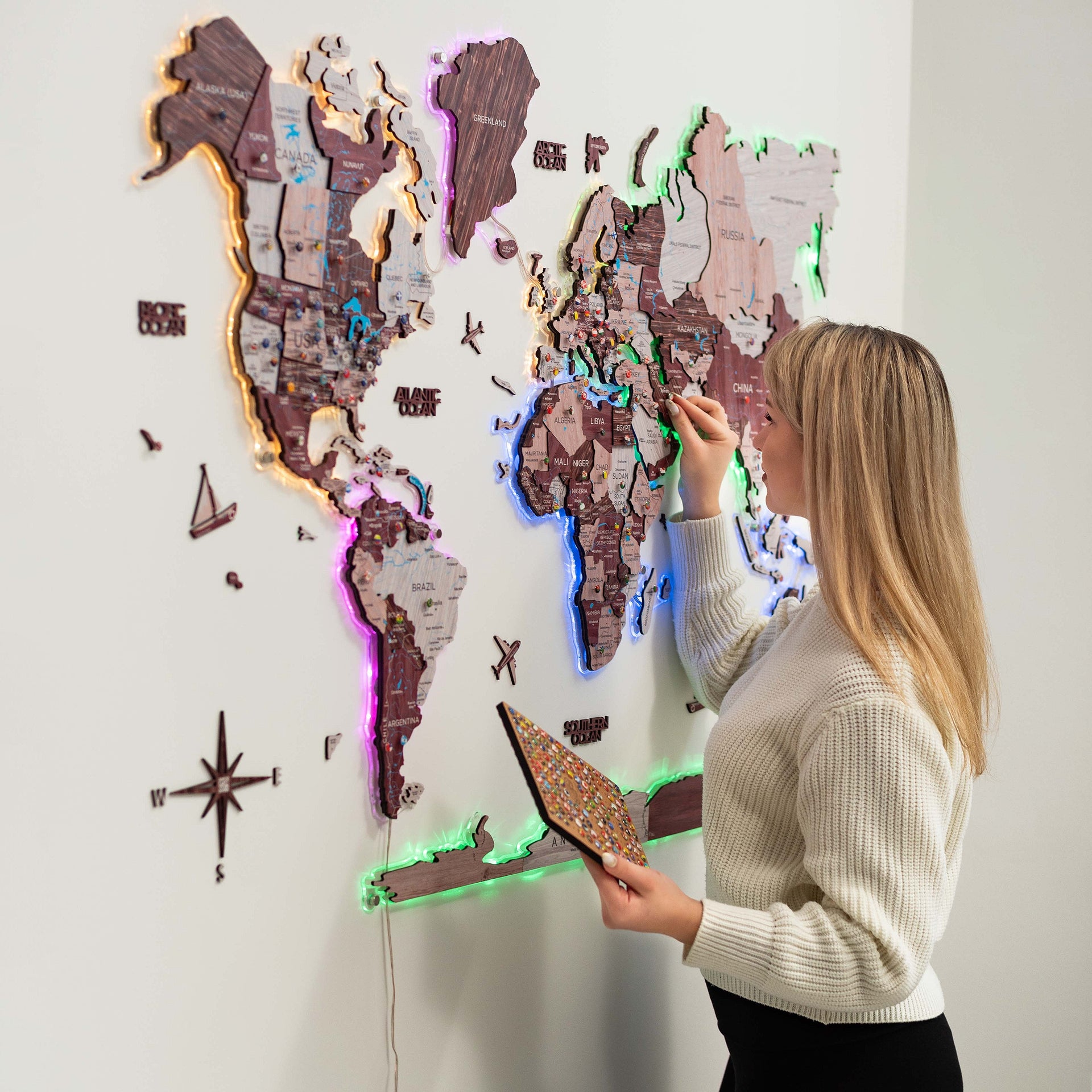 3D Luminous LED Wooden World Map 2.0 in Cappuccino wood tones featuring glowing ambient neon lighting on a modern living room wall.