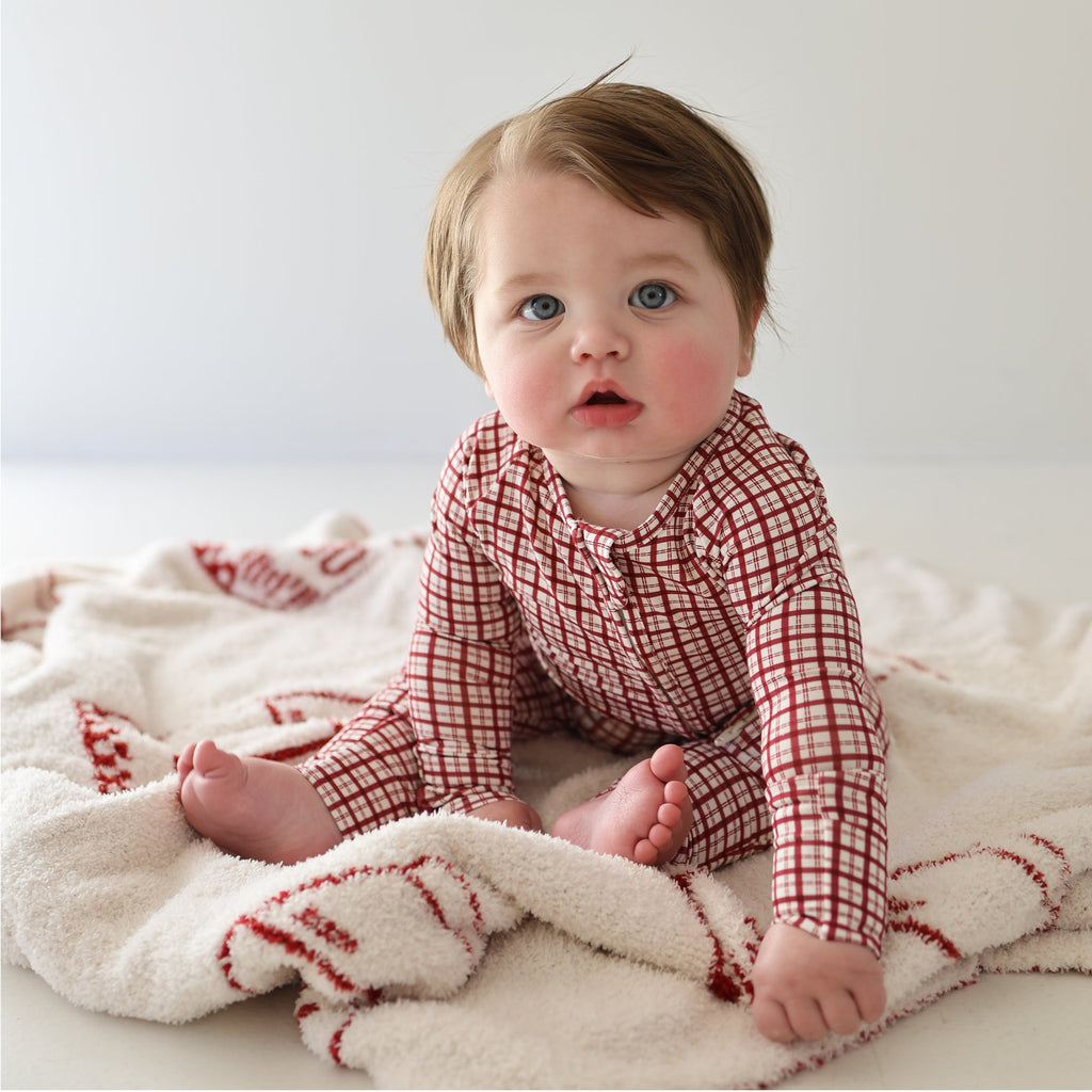 Baby wearing a red and cream window pane print bamboo zip pajama on a white blanket