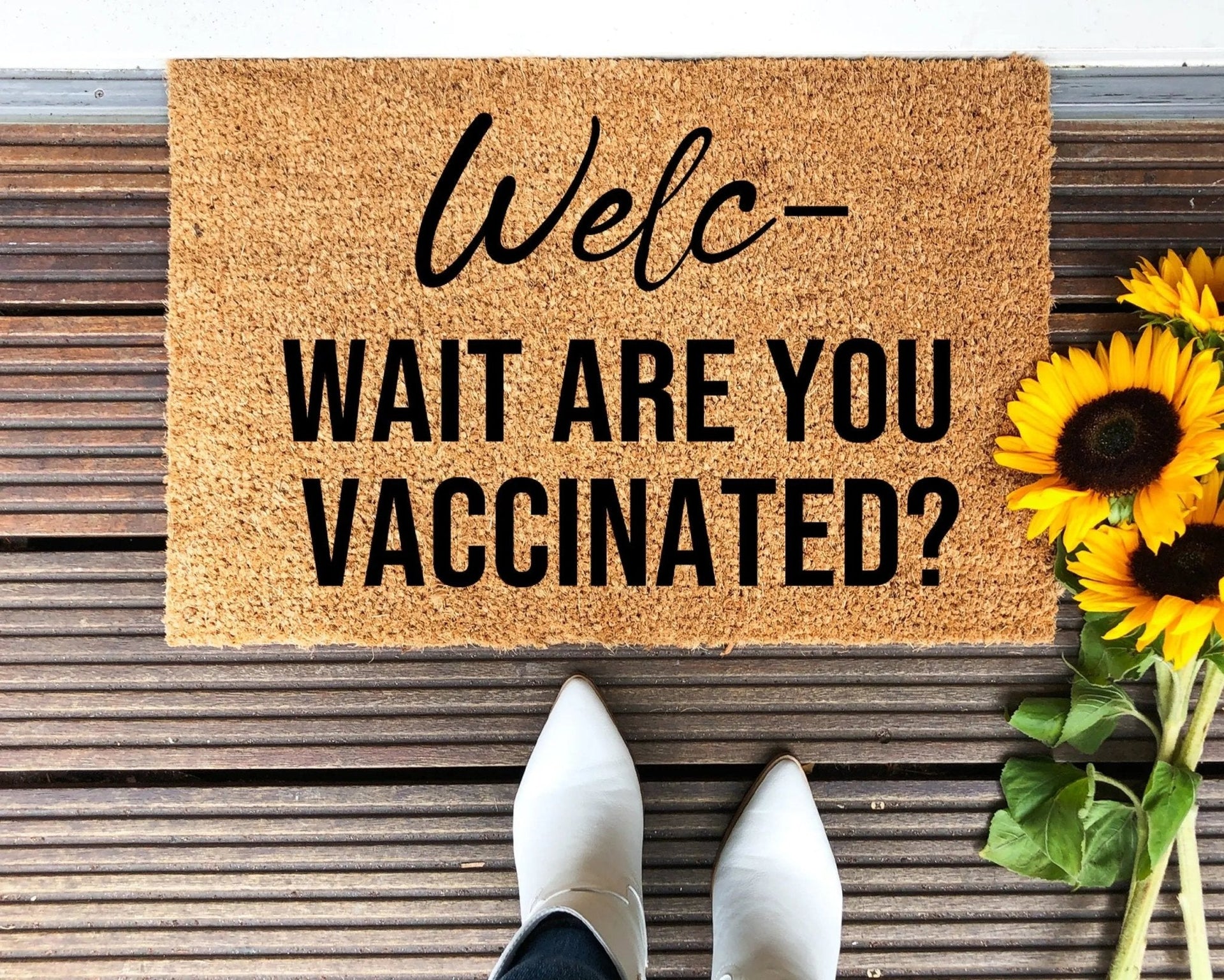 Natural brown coir doormat with black text reading 'Wait, Are You Vaccinated?' on a front porch.