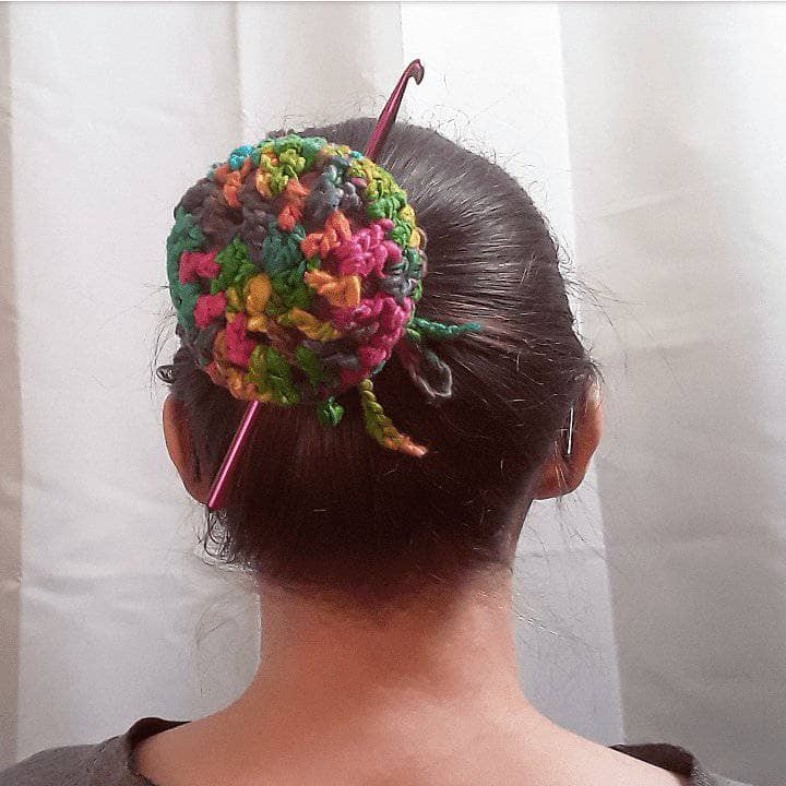 Close-up of a vibrant, knit crochet bun cover acting as a holder for a metal crochet hook in a bohemian style setting.
