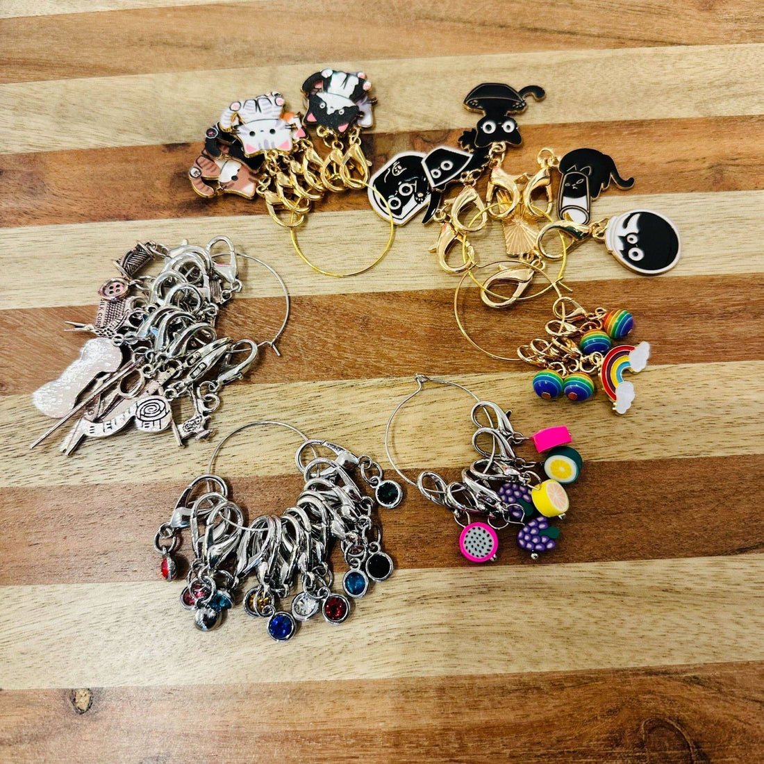 A variety of colorful, whimsical stitch markers including cats, fruits, and rhinestones for knitting and crochet.