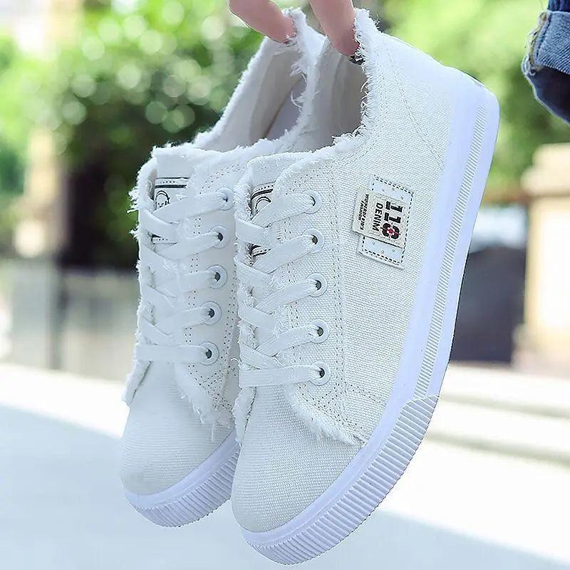 A pair of classic white canvas women's fashion sneakers with white laces and contrasting stitching.