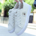 A pair of classic white canvas women's fashion sneakers with white laces and contrasting stitching.