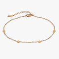 White enameled chain anklet with gold-plated coin stations on a light background
