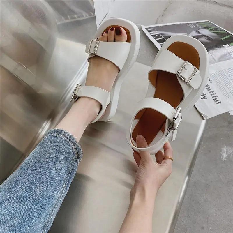 Close-up of elegant white flat sandals for women with a secure buckle strap and rounded toe design