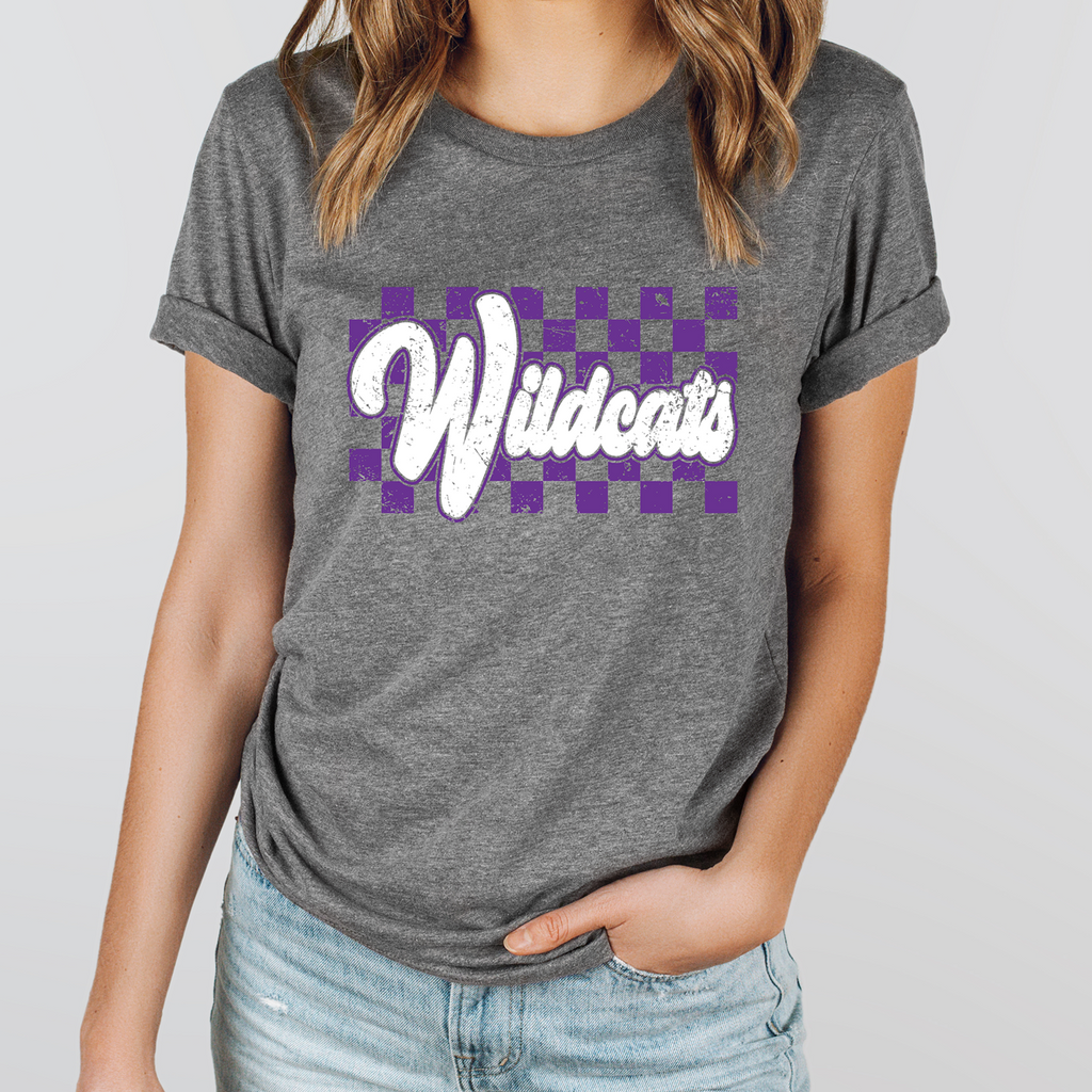 A person wearing a deep heather gray Wildcats graphic t-shirt with a purple and white distressed checker pattern, paired with light wash jeans.