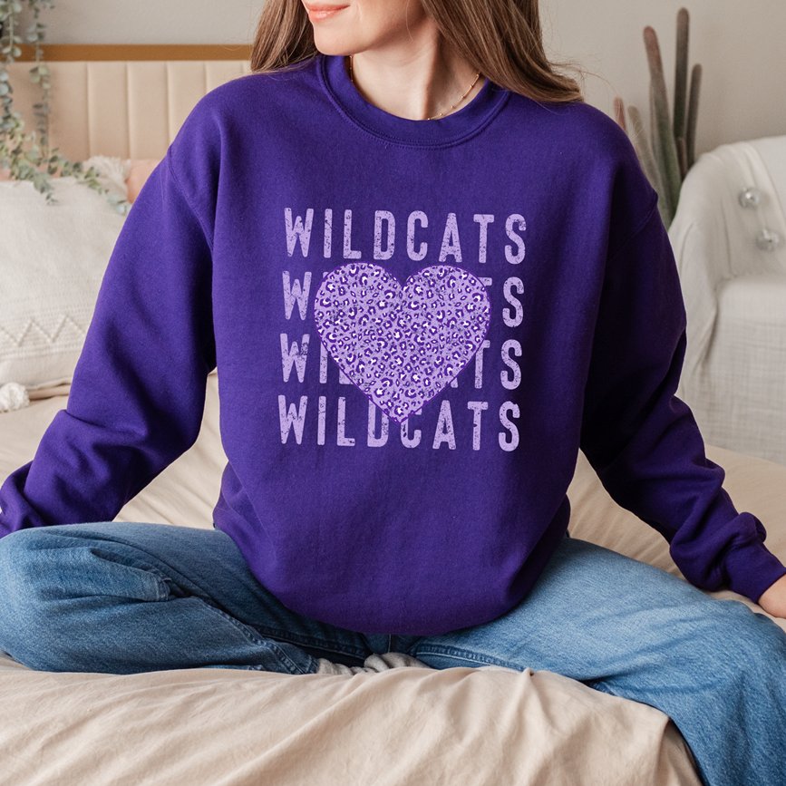 A person wearing a purple sweatshirt with a Wildcats leopard heart graphic design; a flat-lay view of the same design on a purple T-shirt.