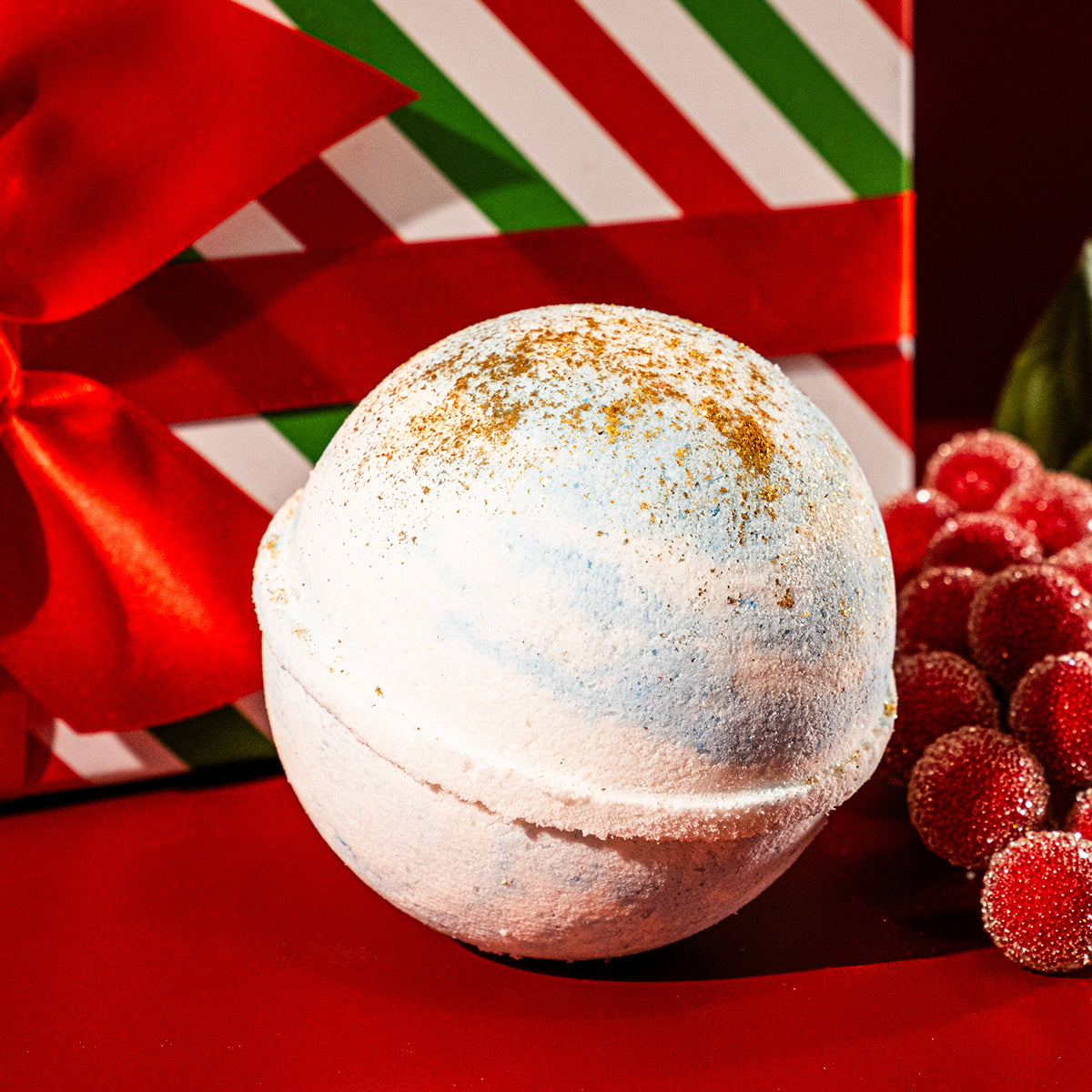 Winter Air jewelry bath bomb with blue and white colors and gold glitter accents sitting in front of a holiday gift box.