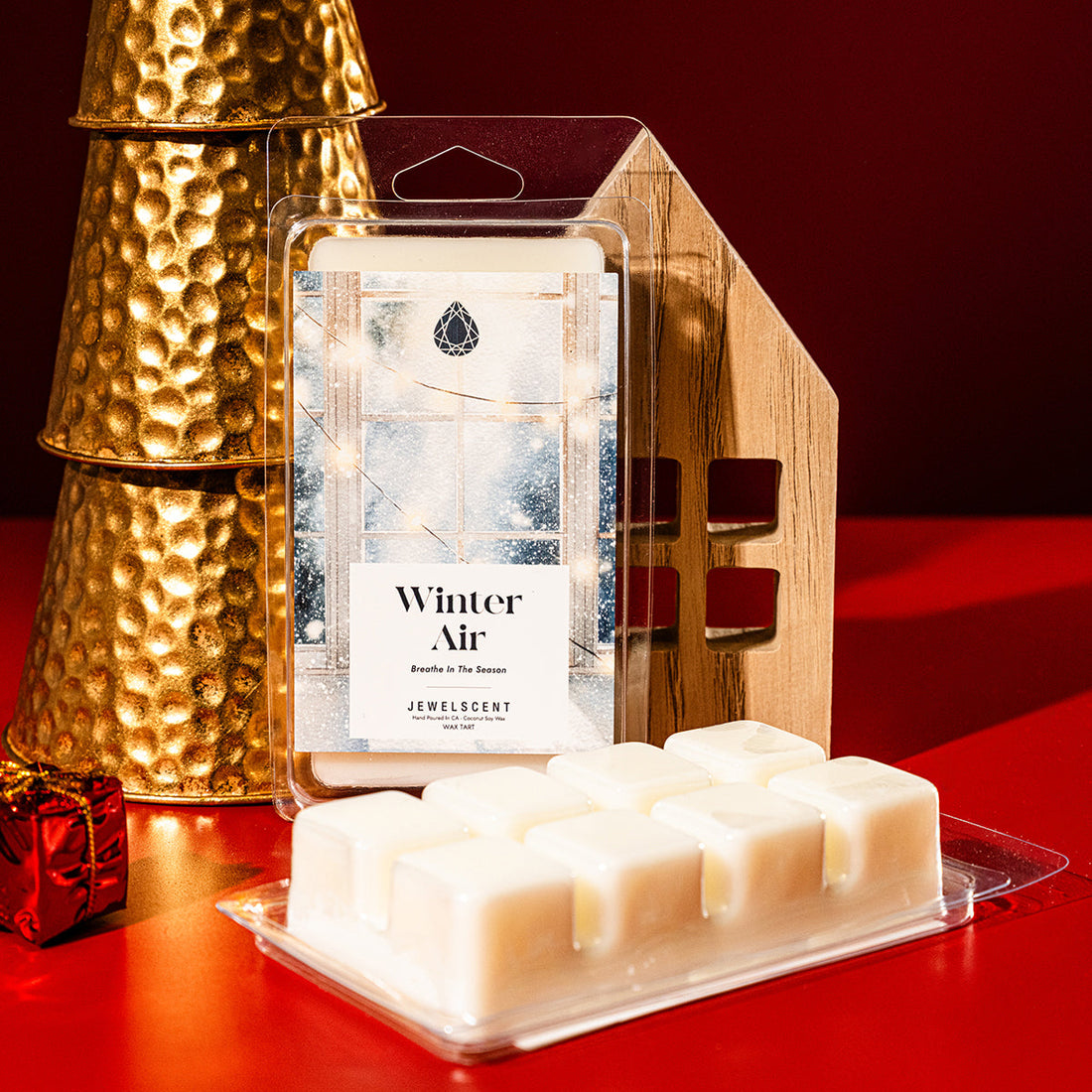 Winter Air scented wax tart packaging in front of gold decorative items and a wooden house cutout