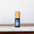 A 10ml amber glass bottle of Komoni Wintergreen Essential Oil with a bamboo wooden cap standing next to its blue cardboard box.