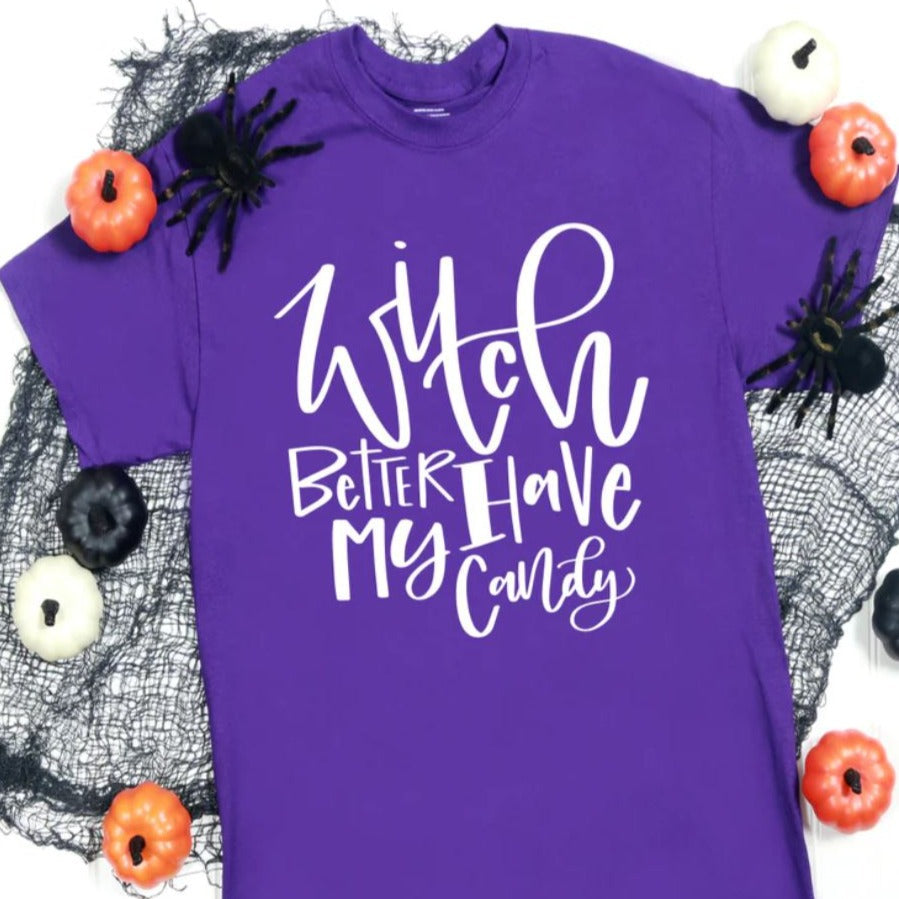 A purple Bella Canvas unisex t-shirt with the white graphic text 'Witch Better Have My Candy' surrounded by Halloween decorations.