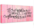 A rectangular canvas wall art piece with a pink faux wood plank background and the black text quote With Grace In Her Heart and Flowers In Her Hair.