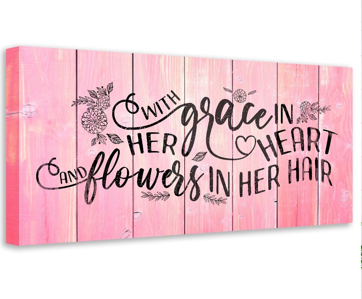 A rectangular canvas wall art piece with a pink faux wood plank background and the black text quote With Grace In Her Heart and Flowers In Her Hair.