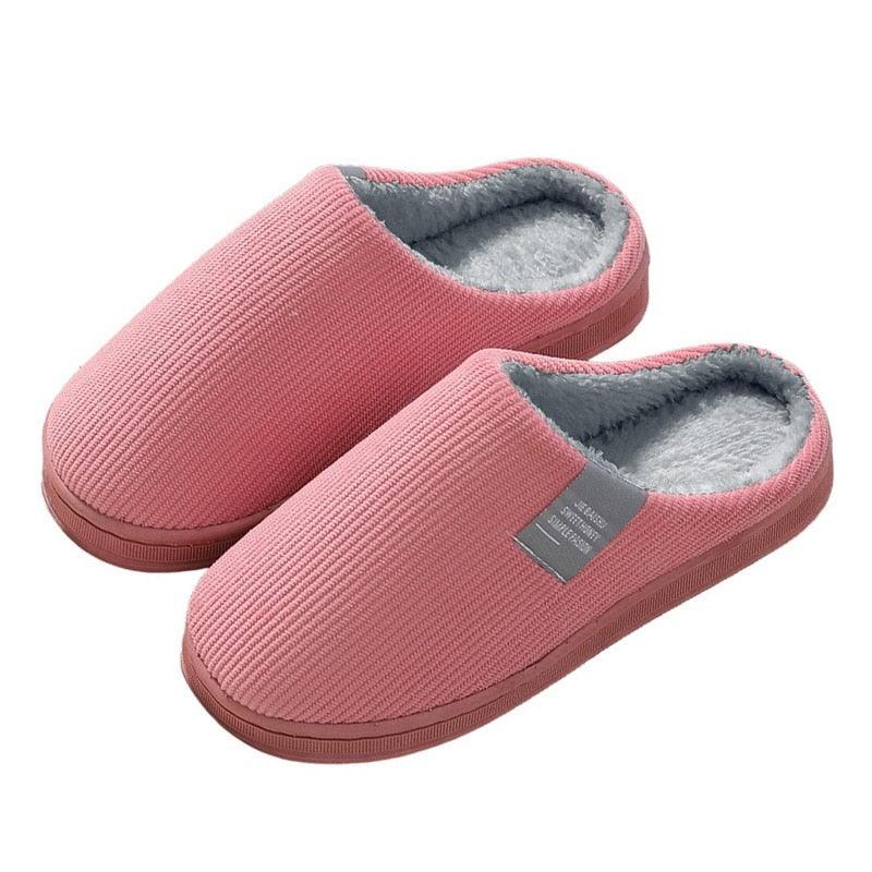 A pair of dusty rose pink knit women's slippers with heather grey lining and anti-skid soles on a minimalist bedroom rug.