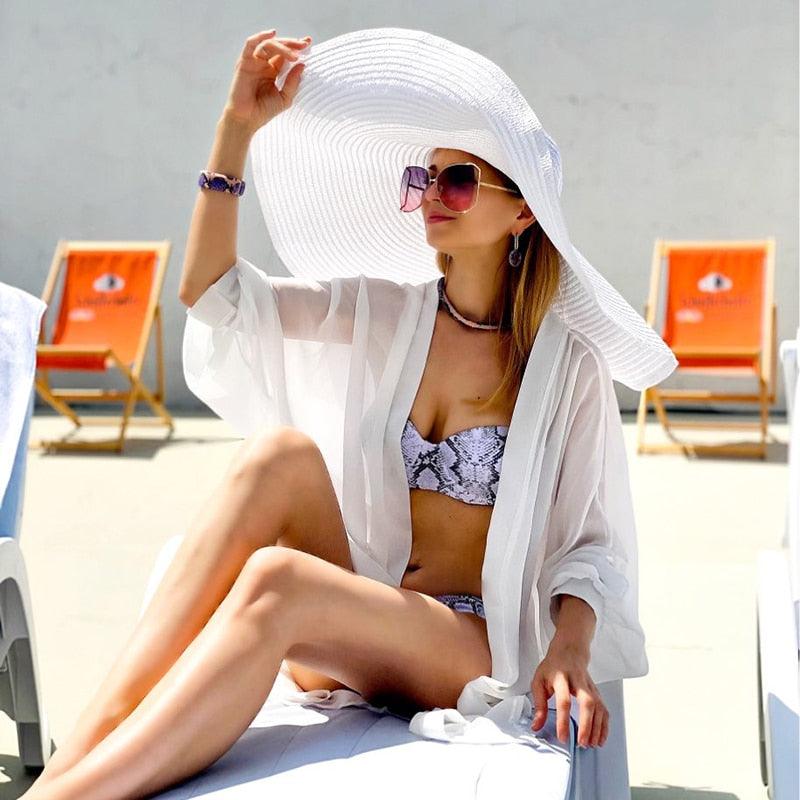 A woman wearing a stylish, oversized foldable straw sun hat with a wide brim on a beach.
