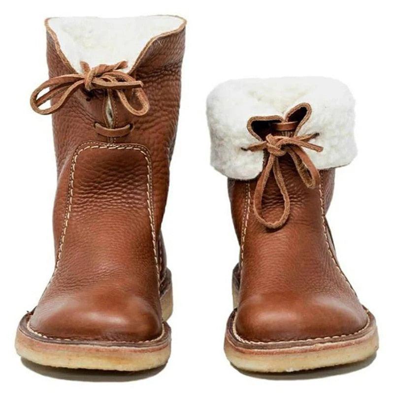 A pair of women's mid-calf leather boots in brown featuring a cream faux-fur interior and tie closure, set against a rustic background.