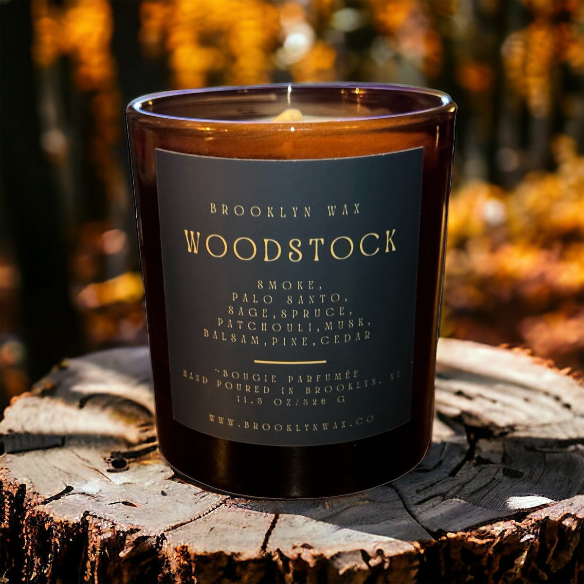 Woodstock 11.5oz scented candle in a dark amber glass jar with a black label, sitting on a natural wood surface.