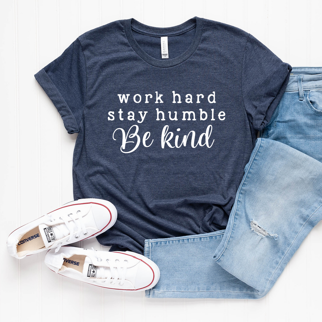 Heather navy unisex crew neck graphic tee with the quote Work Hard Stay Humble Be Kind in white text, laid out with blue jeans and white sneakers.