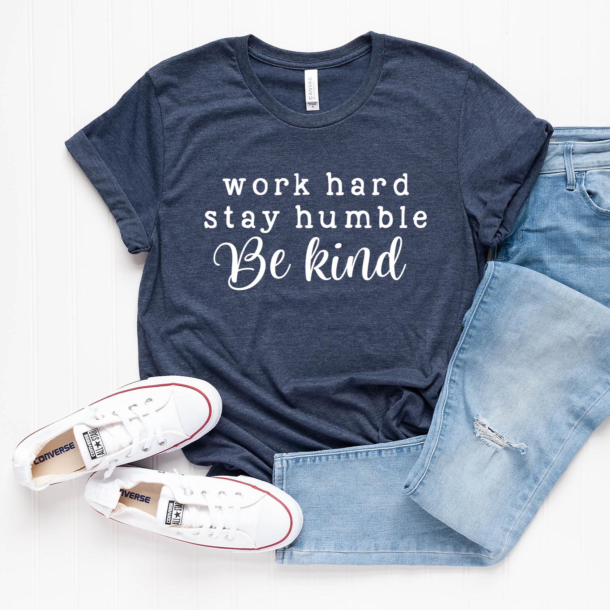 Heather navy unisex crew neck graphic tee with the quote Work Hard Stay Humble Be Kind in white text, laid out with blue jeans and white sneakers.