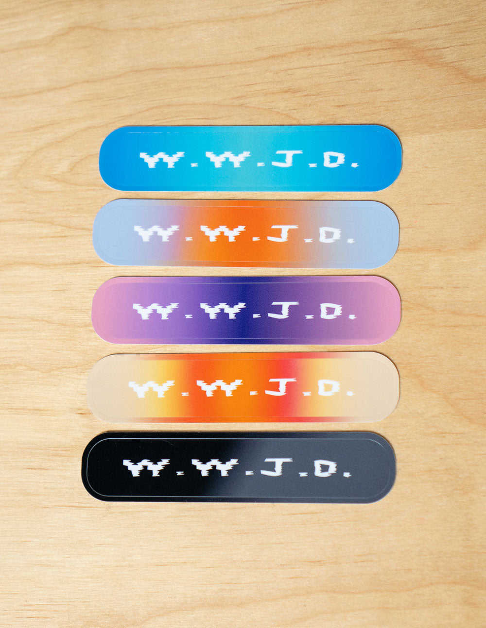 A set of five colorful gradient stickers featuring the text W.W.J.D. on a light wood background, next to a blue phone case.