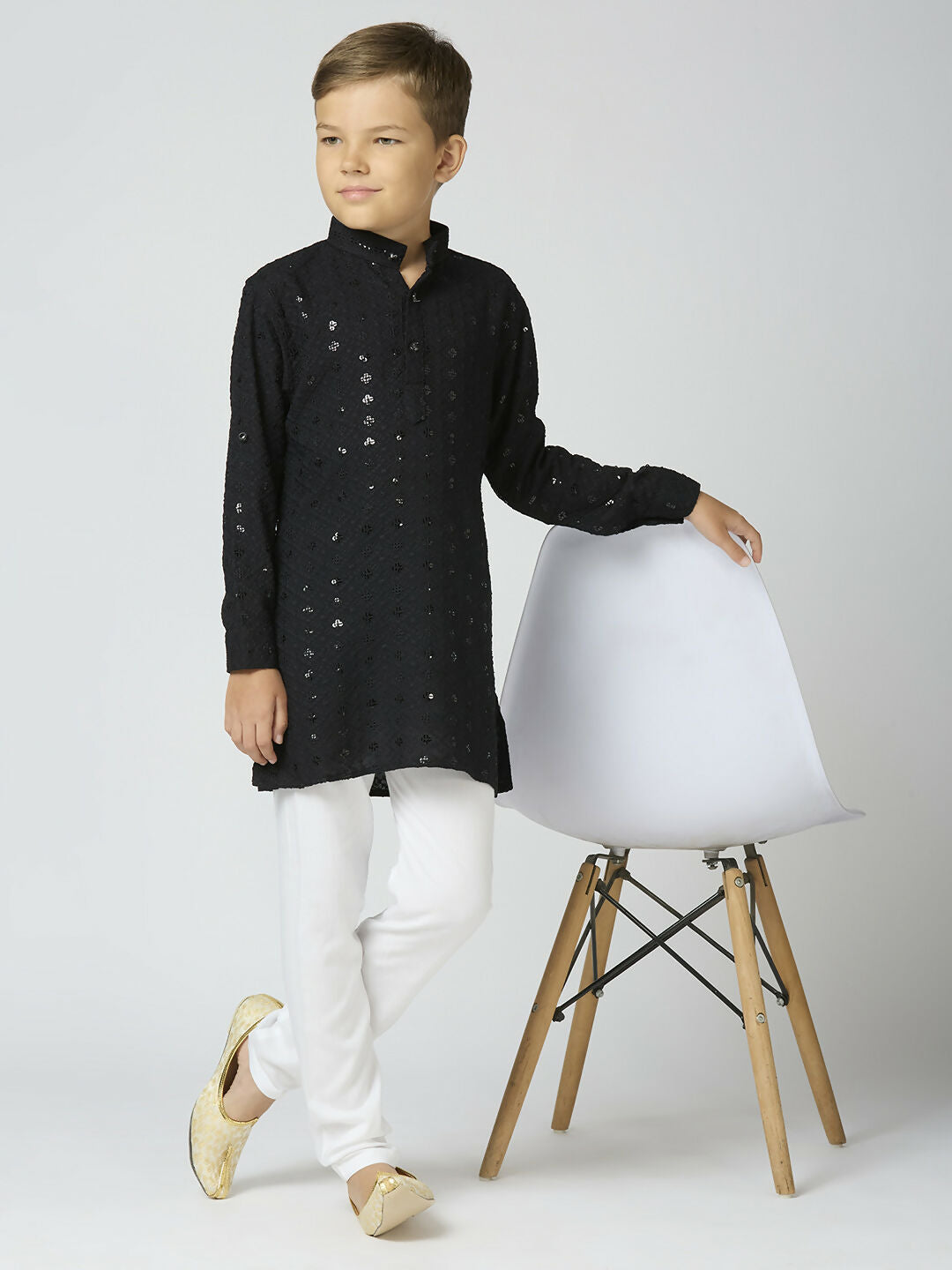 A young boy wearing a black full sleeves cotton kurta and pyjama set with elegant sequin detailing.