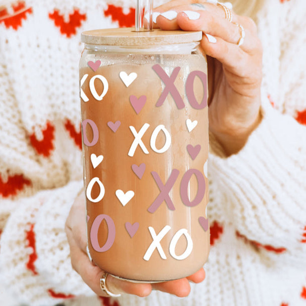 A 20oz glass cup with a bamboo lid and glass straw, featuring a pink and white XOXO heart pattern.