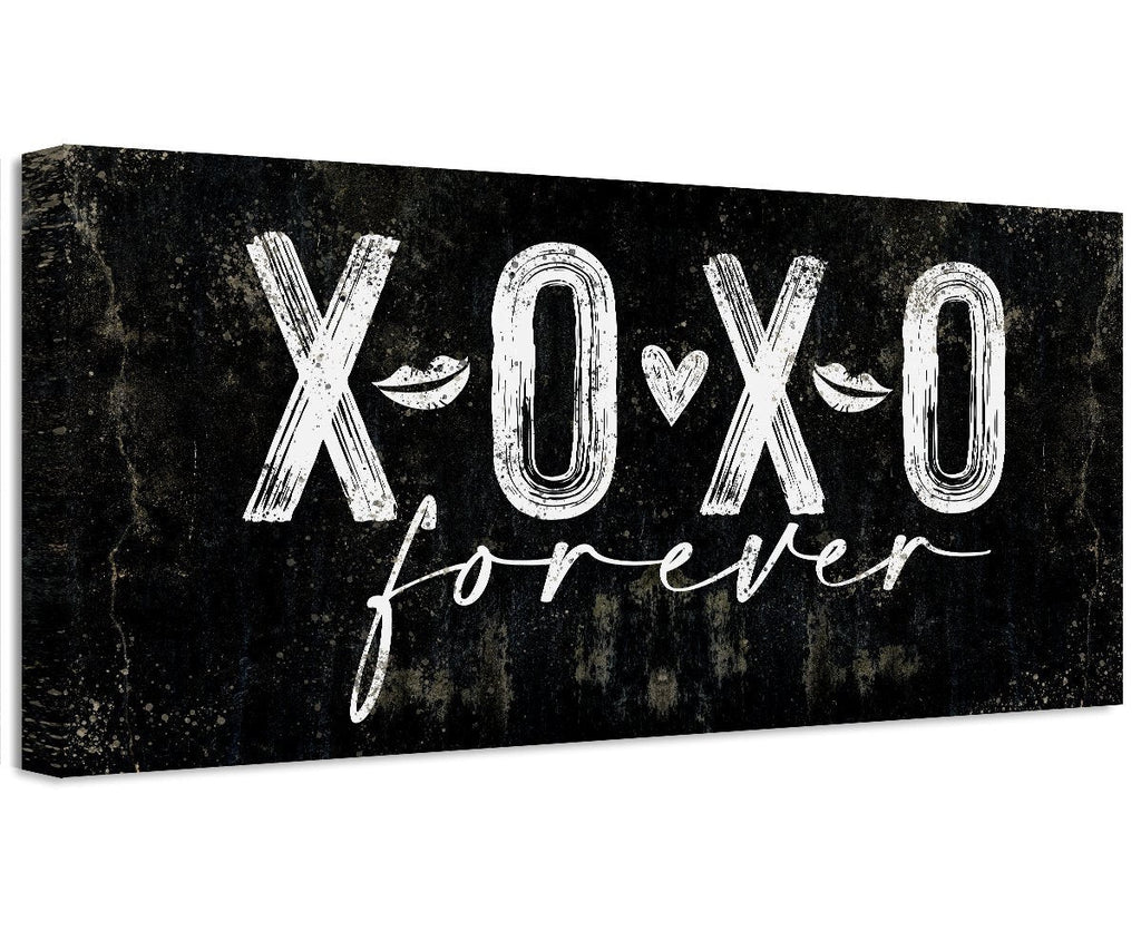 A black and white canvas print displaying XOXO Forever text, hanging above a bed as wall decor.