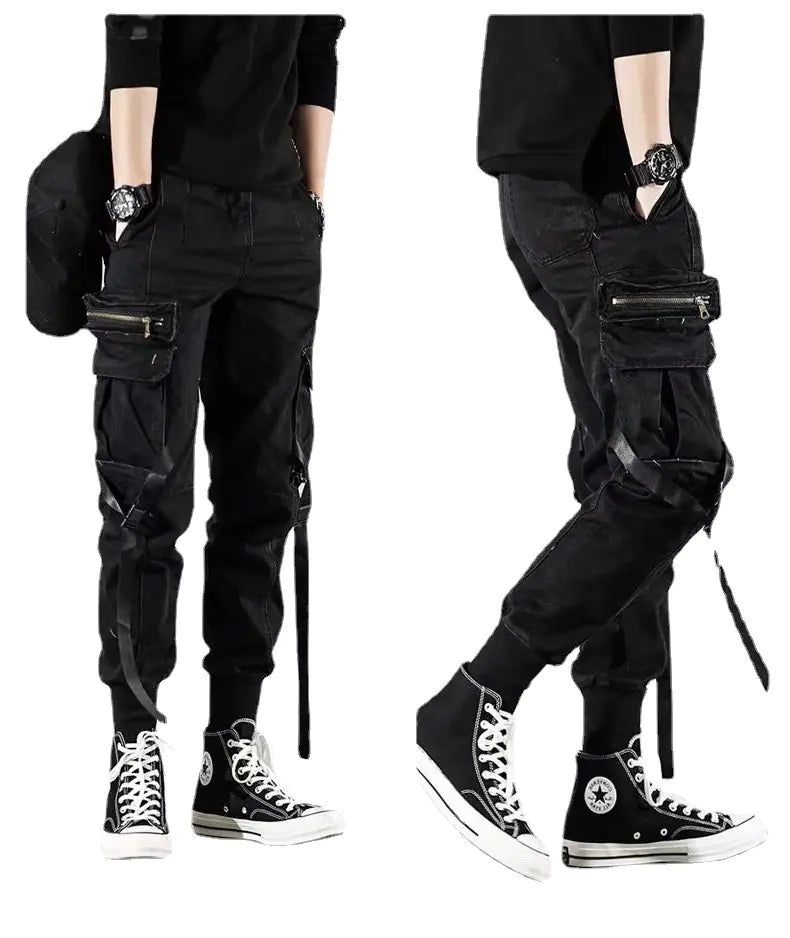 A person wearing black tactical paratrooper cargo pants with multiple pockets, hanging streamers, and cuffed ankles, paired with high-top sneakers.
