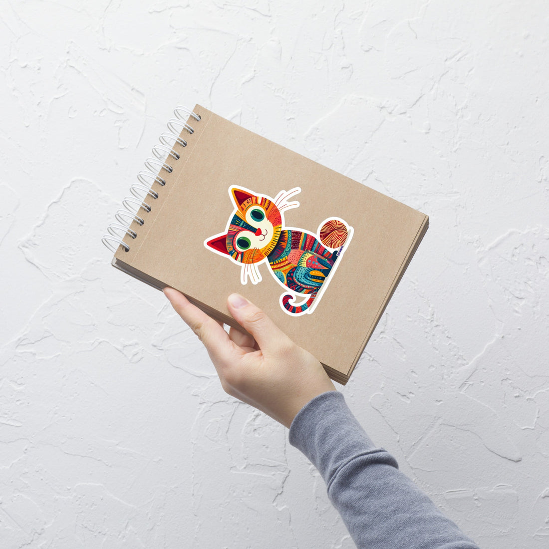 A whimsical vinyl sticker featuring a cute cat made of knitted and crocheted textures with a ball of yarn, designed by Nicole Snow.